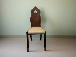 A dark wood back dining chair with a soft beige cushion, shown against a white brick wall on a grey floor.