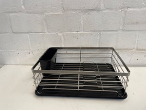 A black dish rack with adjustable compartments placed against a white brick background.