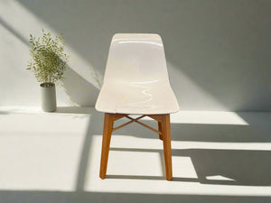 A white plastic dining chair with wooden legs, positioned against a white brick wall on a black floor, showing slight cracks on the seat.