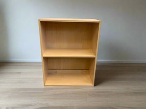 A wooden bookshelf with two shelves against a white brick wall background.