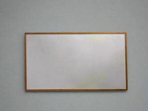 A grey wooden framed notice board with a cracked texture, leaning against a white brick wall.