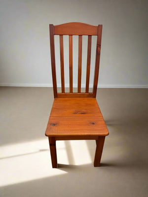 A single wooden dining chair with a straight back and seat, positioned against a white brick wall on a patterned floor.