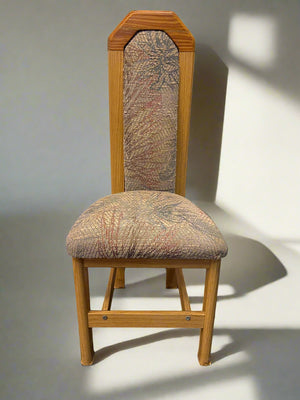 A mid-century styled wooden dining chair with patterned fabric seating against a white brick background.