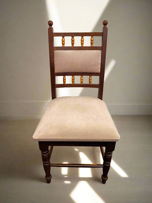 A classic wooden dining chair with a beige upholstered seat and a rich brown finish on the wood, featuring decorative spindles on the backrest.