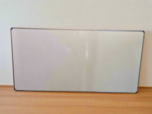A whiteboard with an aluminum frame, positioned upright against a wall, with minor scuffs visible on the frame.