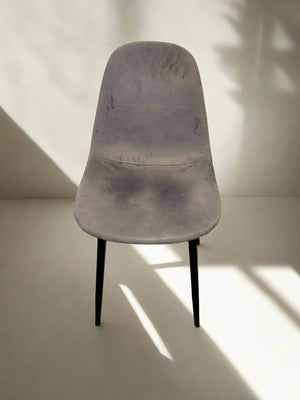 A gray fabric chair with black metal legs against a white brick wall, showing minor wear.