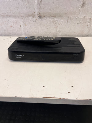 Black DStv decoder with remote on a white surface against a gray wall.