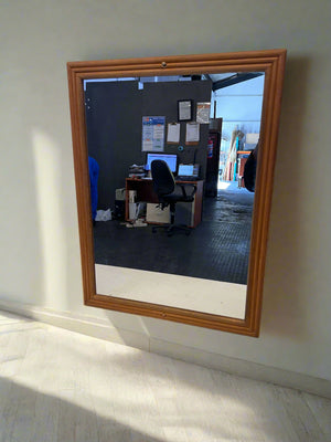 Wooden-framed mirror on a wall reflecting an office desk with computers.