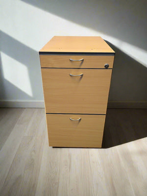 Wooden file cabinet with three drawers on a light wooden floor.