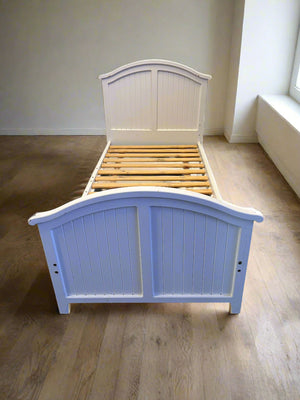 White wooden bed with slatted headboard on a wooden floor.