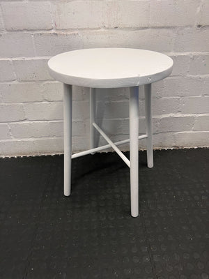 Round white table with four legs on a black floor against a gray brick wall.