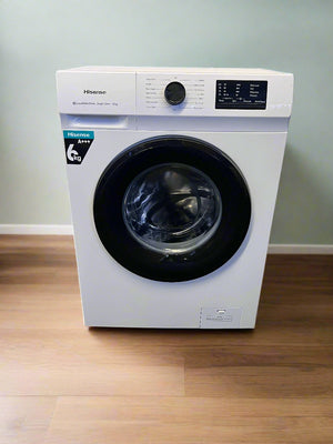 White washing machine with black door on a gray floor against a light gray brick wall.