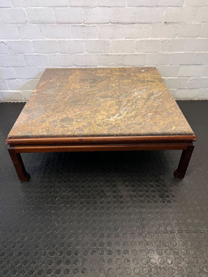Square coffee table with a textured surface on a black floor against a white brick wall.