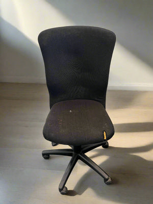 Black office chair on a light wooden floor with a white wall background