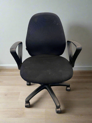 Black office chair on a wooden floor with a plain wall background