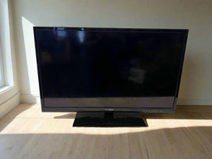 Black flat-screen TV on a wooden floor with a light-colored wall background