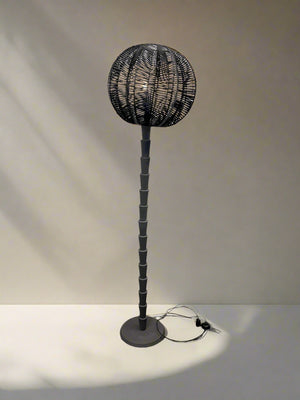 Black floor lamp with wicker design against a white brick wall.