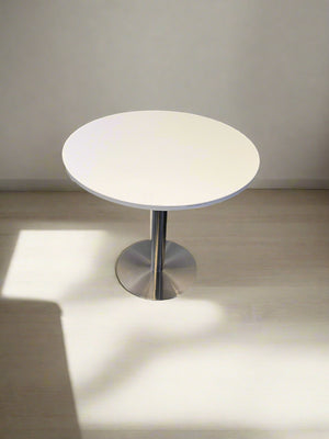 Small round table with a white top and metallic base on a neutral background