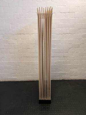 Tall, cylindrical wooden object with slits against a white brick wall.