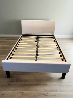 White bed frame with wooden slats against a white brick wall.