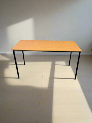 Wooden table with black legs on a tiled floor and white wall background