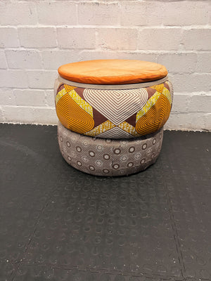 Two fabric-covered stools with patterned tops and a plain bottom, stacked against a gray brick wall.