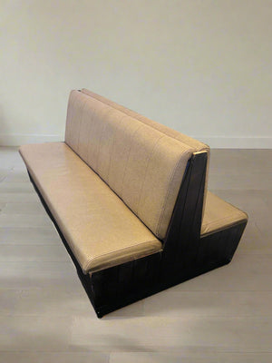 Beige and black bench against a white brick wall.