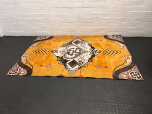 Decorative rug with geometric pattern on a black floor against a white brick wall.