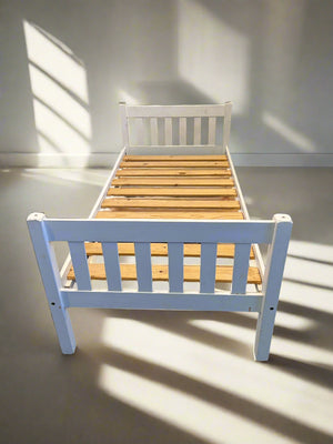 White wooden single bed frame with slats, positioned against a white brick wall on a black surface.