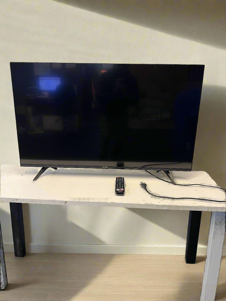 Flat-screen TV on a stand with a remote control and cable in a room.