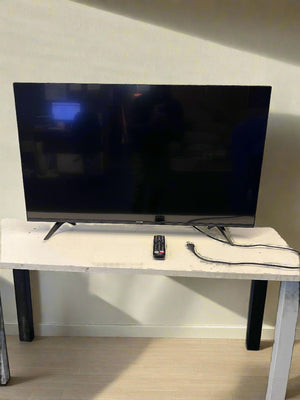 Flat-screen TV on a stand with a remote control and cable in a room.