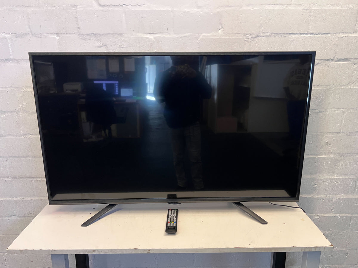 Flat-screen TV on a stand with a remote control in front of a brick wall.