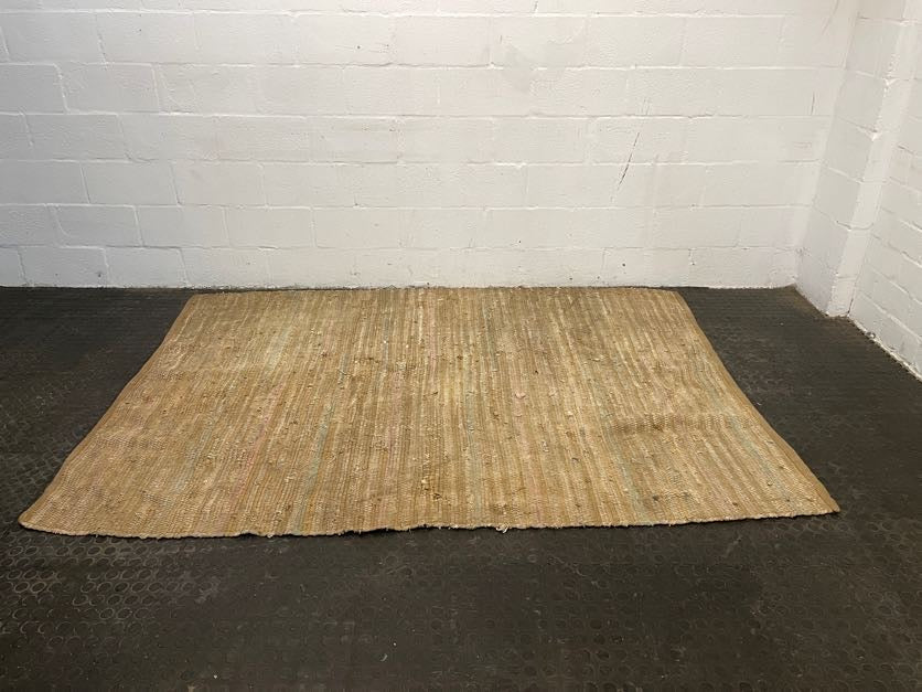A light brown woven rug laid out on a black floor, with a plain white wall in the background.