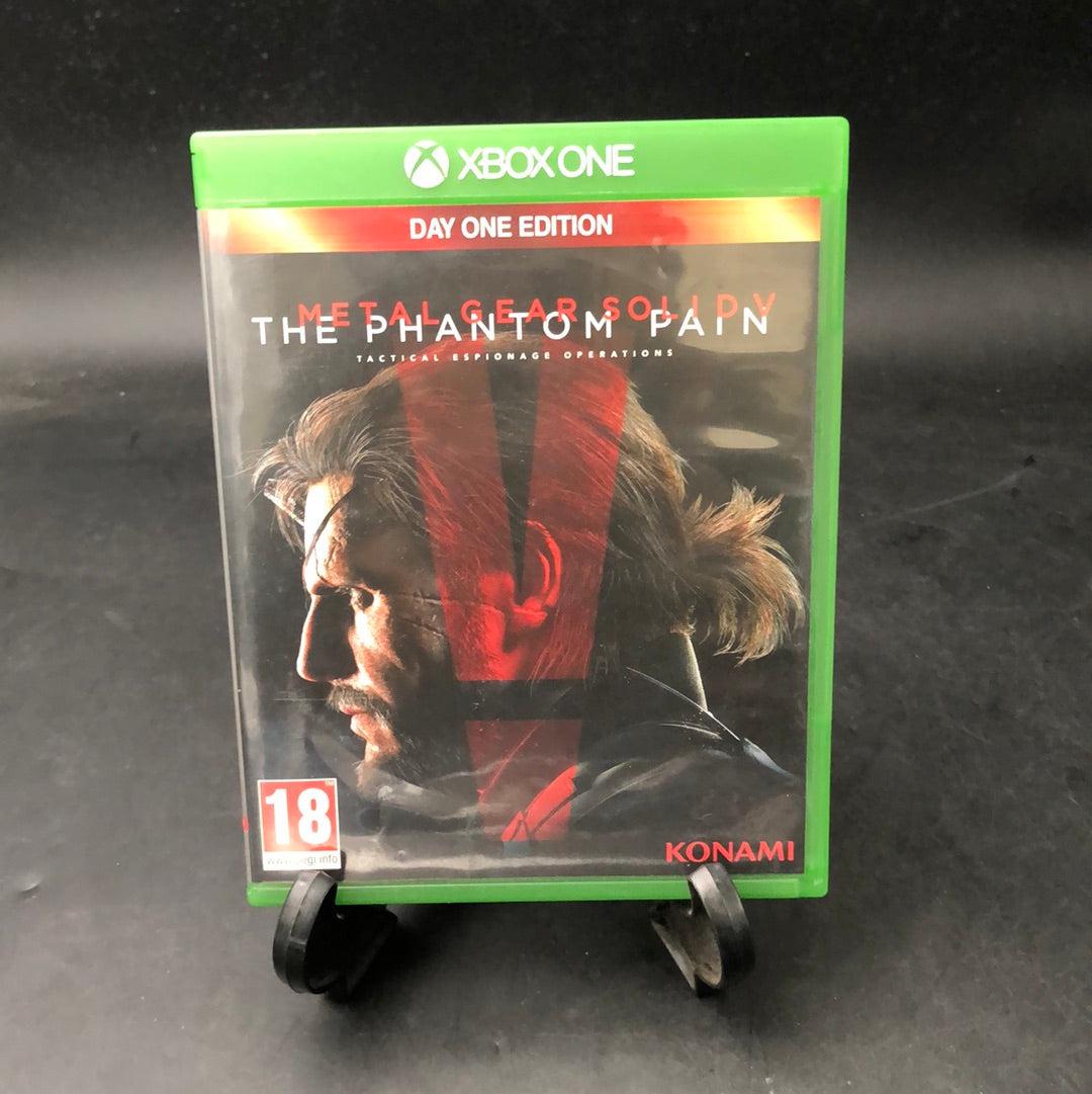 A copy of Metal Gear Solid 5 - The Phantom Pain for Xbox One, displayed in a stand, with a 'Day One Edition' label and a '18+' age rating sticker.