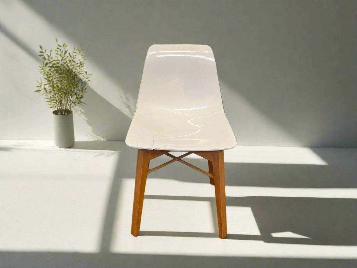 A white plastic dining chair with wooden legs, positioned against a white brick wall on a black floor, showing slight cracks on the seat.