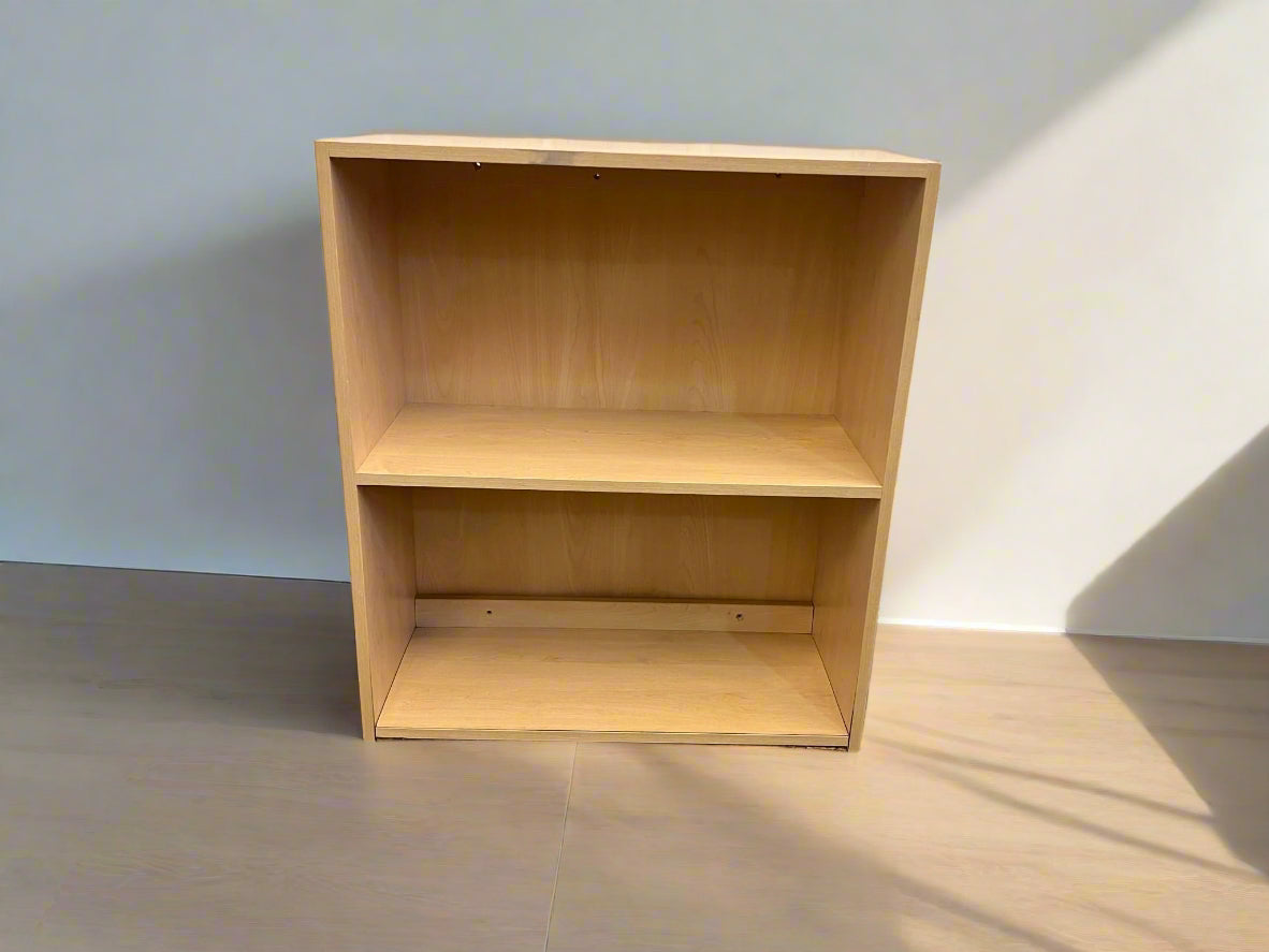 A wooden bookshelf with two shelves against a white brick wall on a concrete floor, reduced in price.