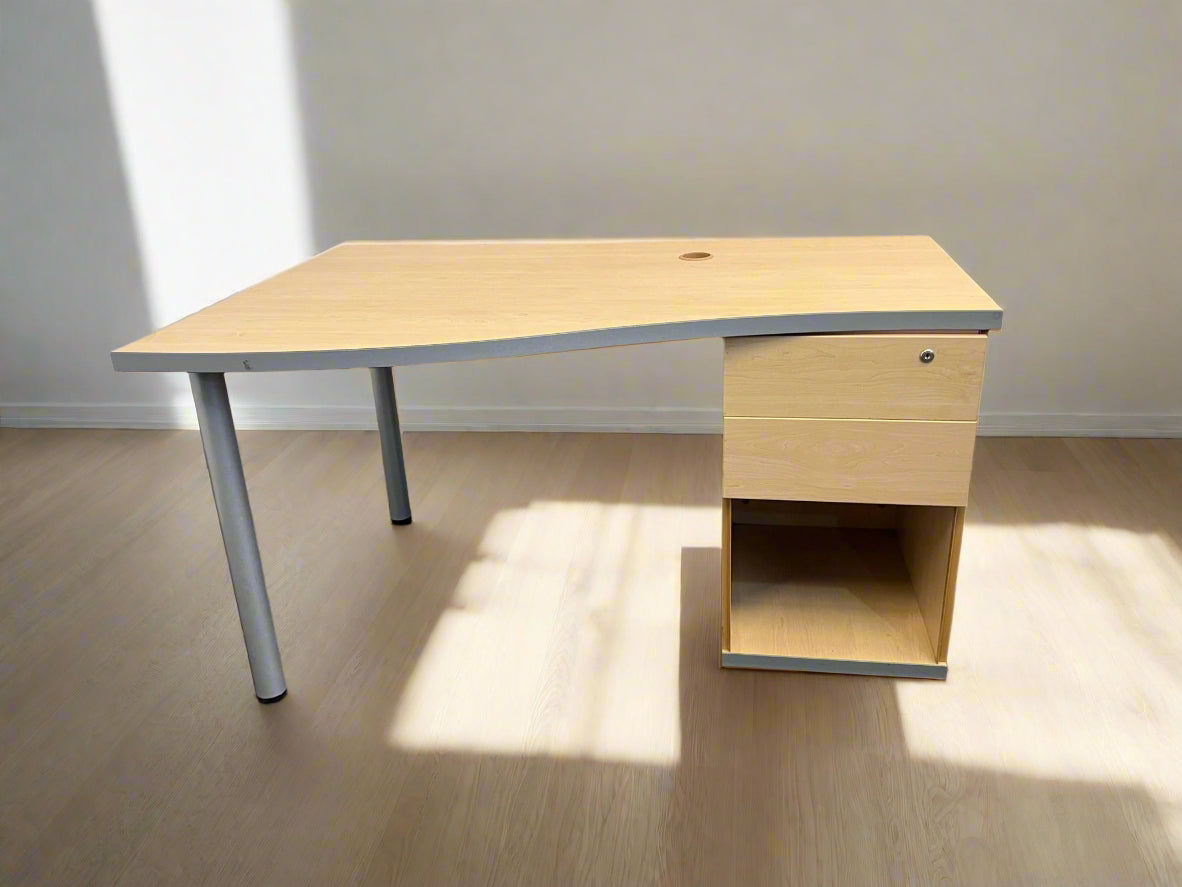 A wooden desk with a gray metal leg and a matching wooden creditena with a lower shelf, placed against a white brick wall on a black grate floor.