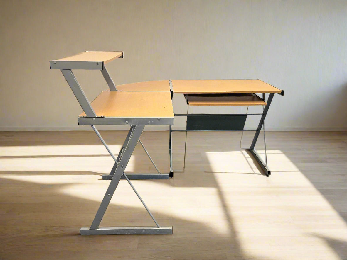 An L-shaped desk with a light wood print top and a steel framed structure, including a keyboard tray and a printer shelf.