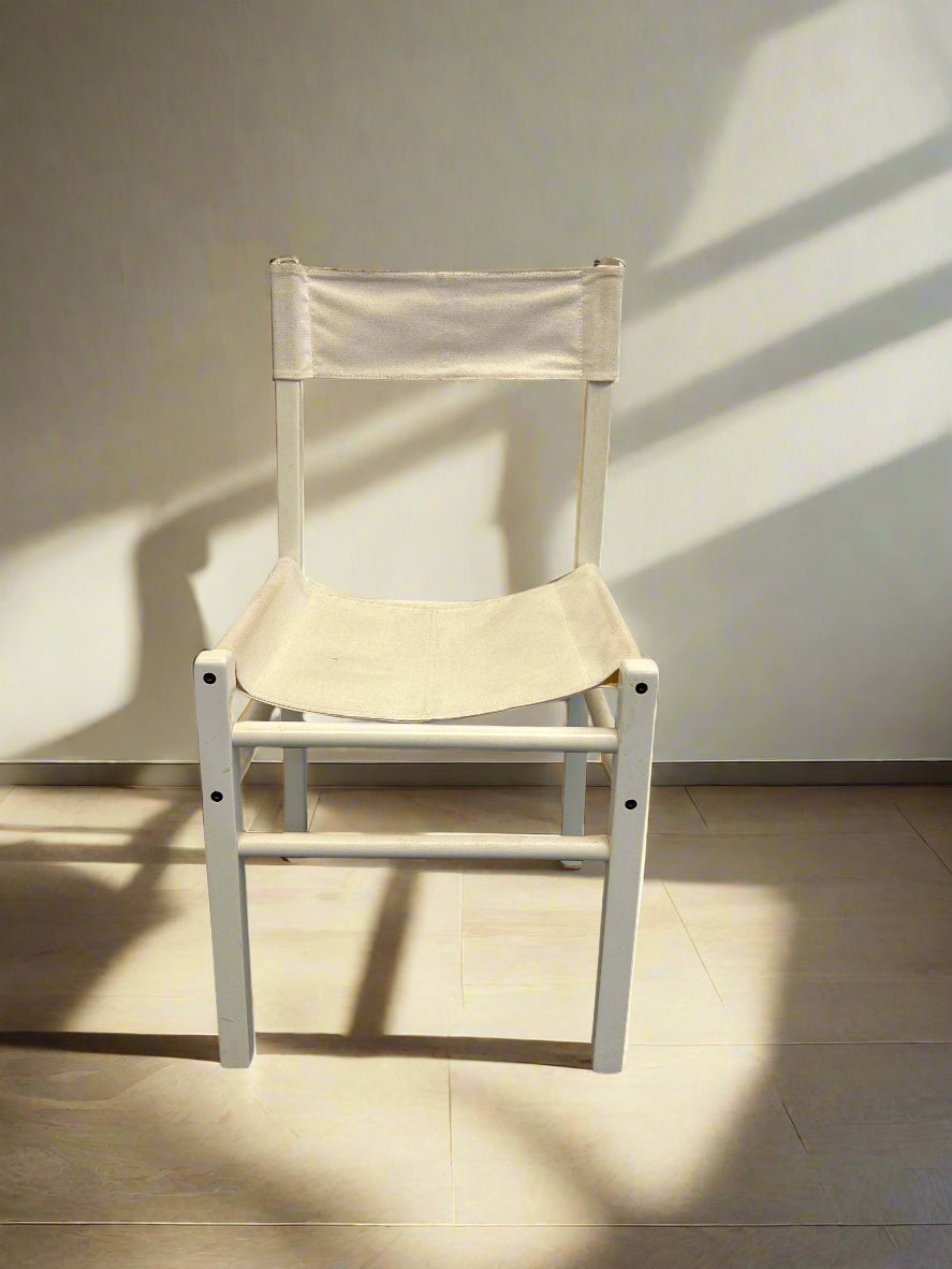 A white wooden dining chair with a fabric seat and backing, displayed against a white brick wall.