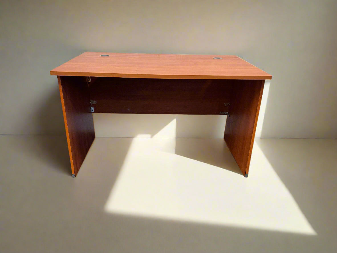 A wooden office desk with scratches, positioned against a white brick wall on a black rubber floor, measuring 120cm in width and 71.5cm in height.