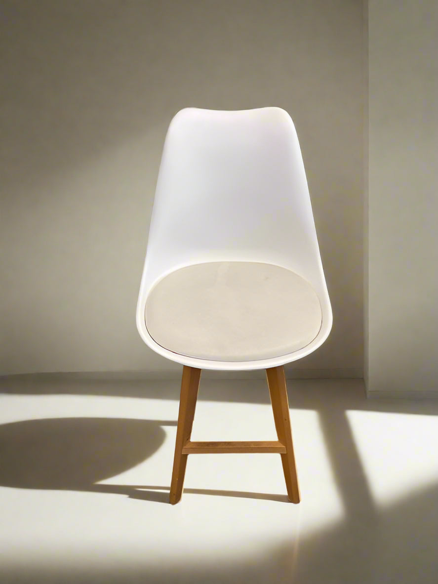 A white cushioned dining chair with a wooden frame and a white brick wall in the background.