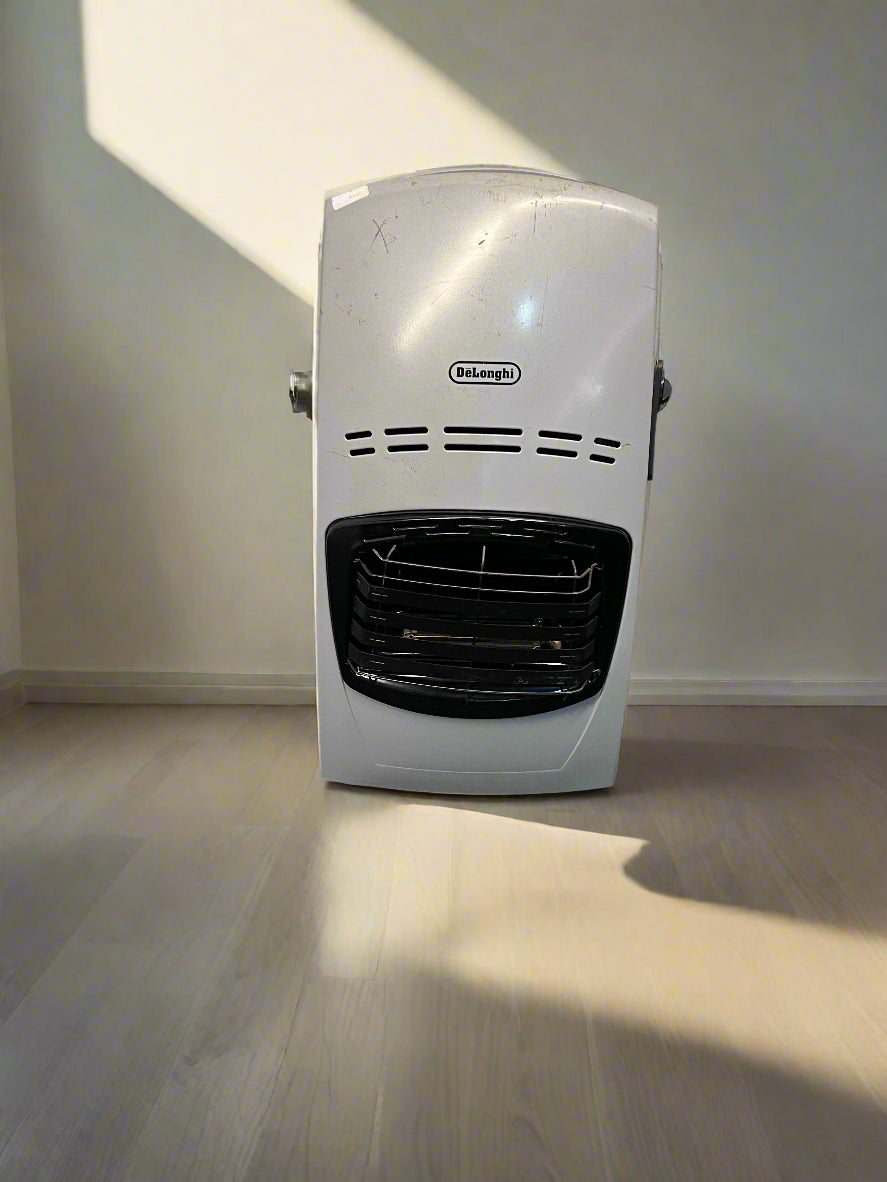 A compact DeLonghi silver heater with minor scratches, positioned against a white brick wall on a dark textured surface.