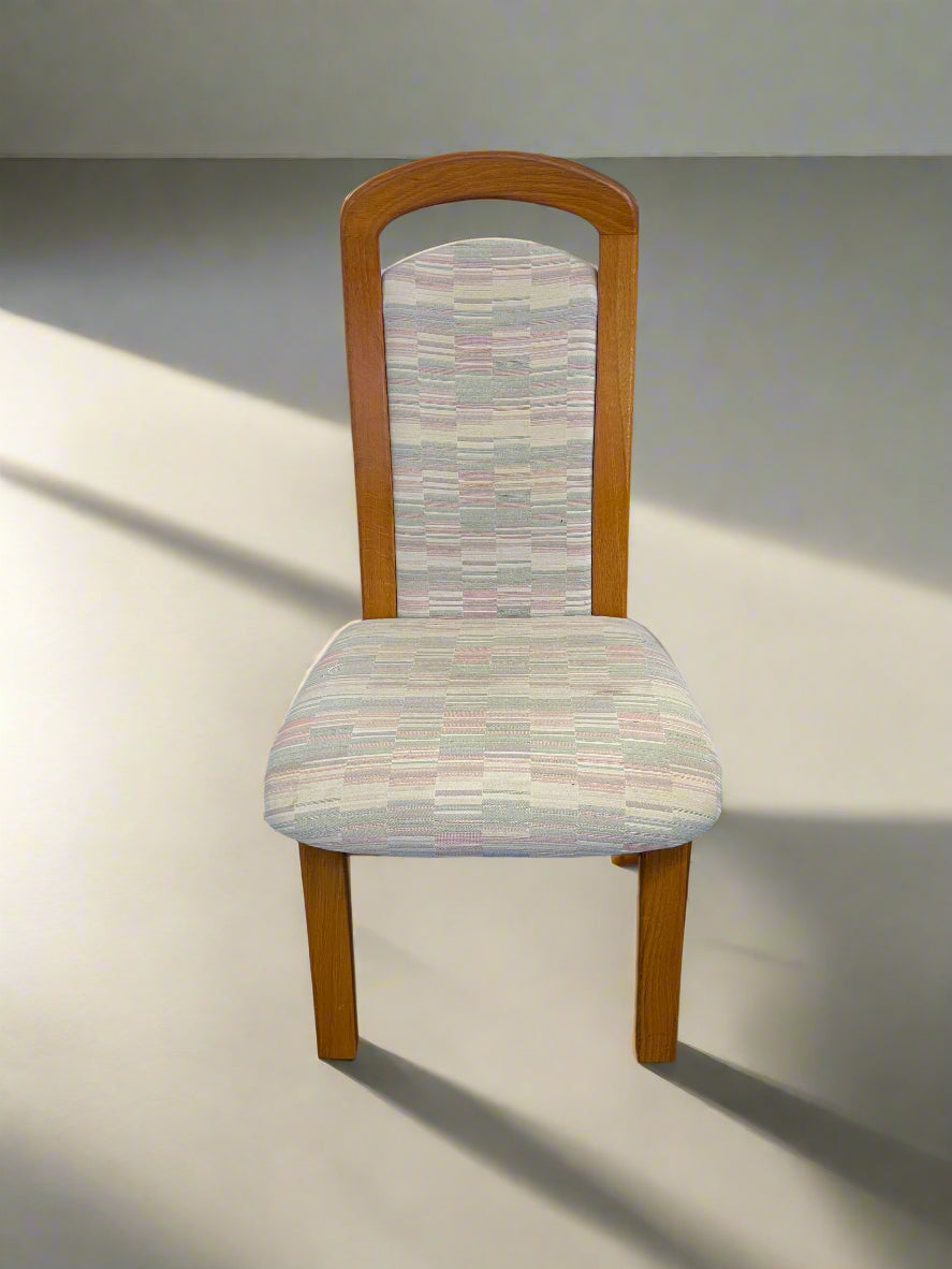 A wooden dining chair with multicolored upholstered seat against a white brick background.
