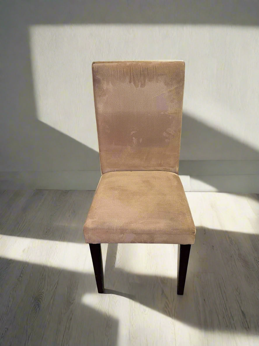 A beige upholstered dining chair with a wooden frame and fabric seating, displayed against a white brick background.