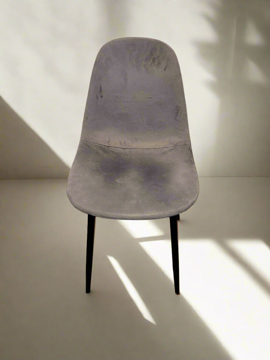 A gray fabric chair with black metal legs against a white brick wall, showing minor wear.