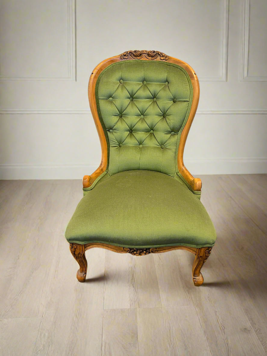 A vintage green upholstered accent chair with a carved wooden frame, viewed from a slight angle against a white brick background.