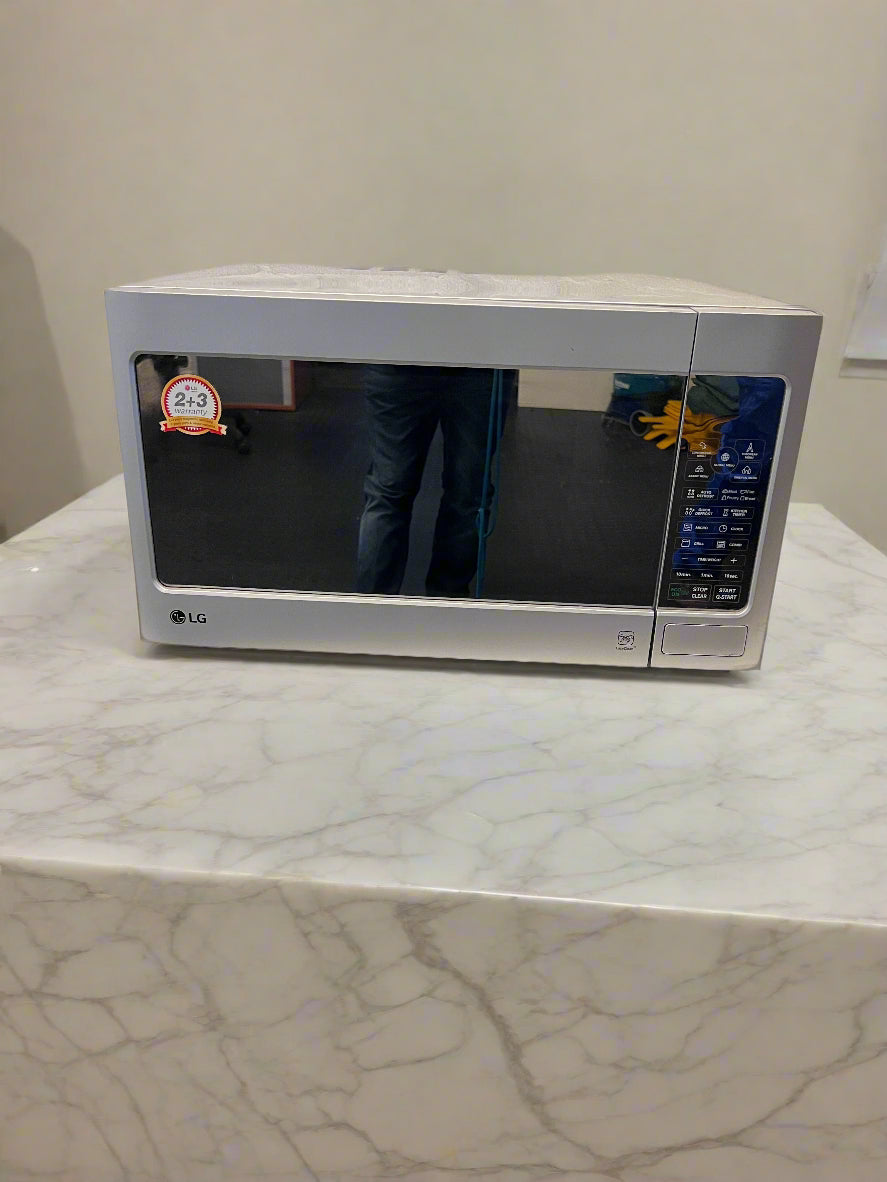 Silver LG microwave on a white surface with a gray brick wall background