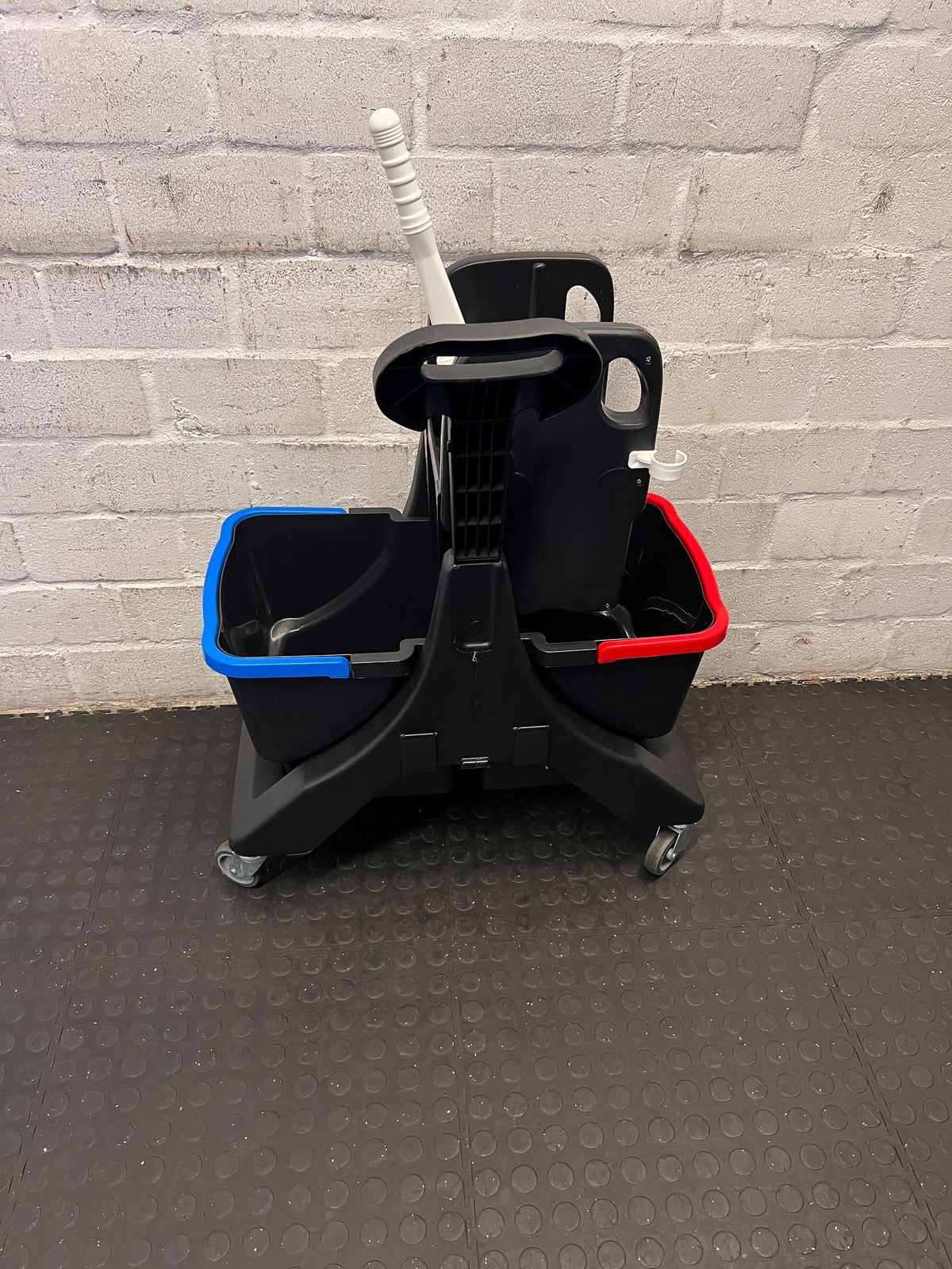 Cleaning cart with buckets and mop against a gray brick wall.