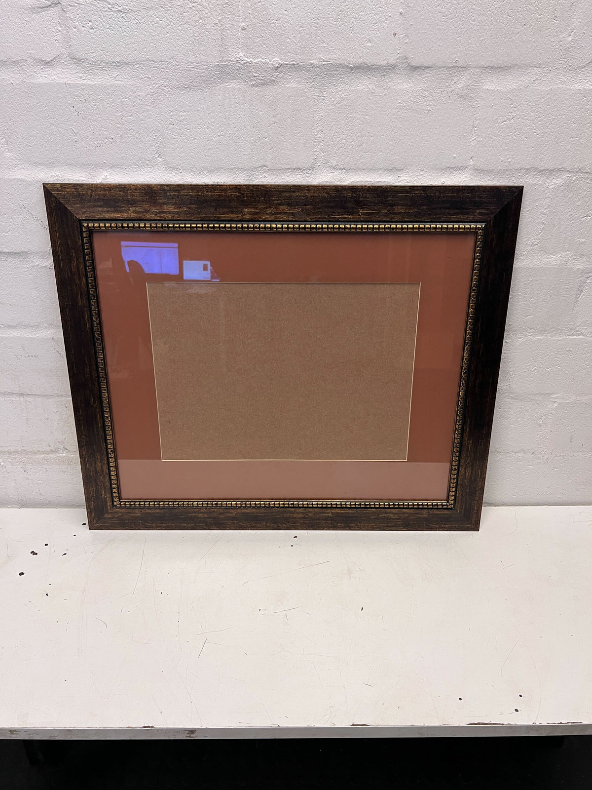 Wooden picture frame with a brown mat on a white surface and light gray wall background