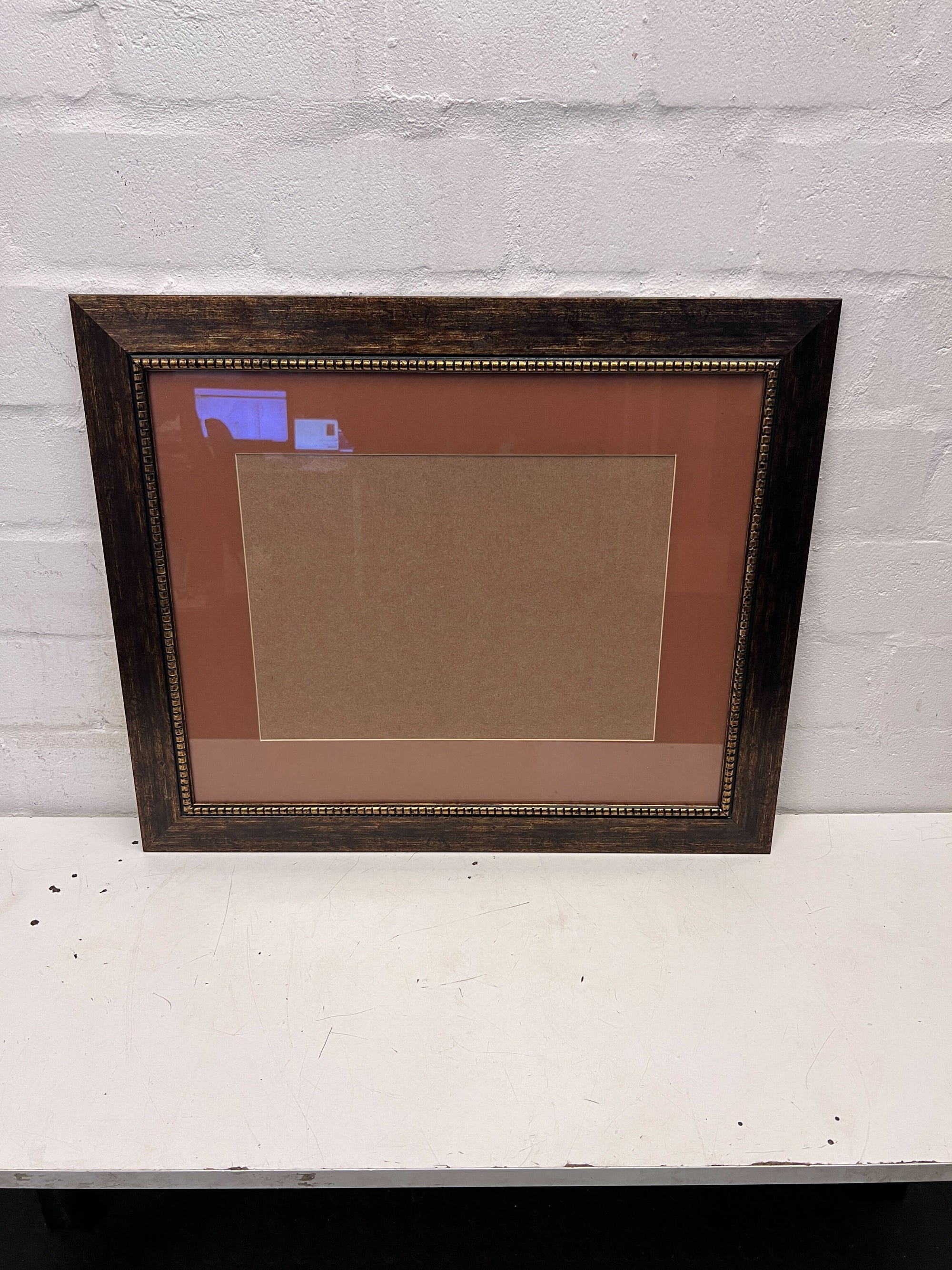 Wooden picture frame with a brown mat on a white surface and light gray wall background